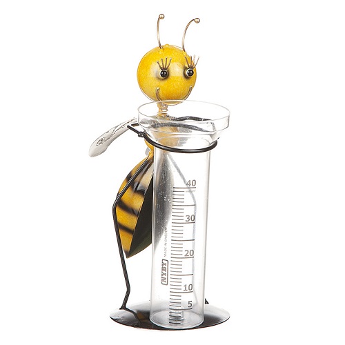 Regnmätare som står på en platta med hål i i sig för att spikas fast. Regnmätarglas med upp till 40ml. Ett bi står på två ben och håller om regnmätarglaset. Biet är guld och svart med guldiga antenner och vita vingar.